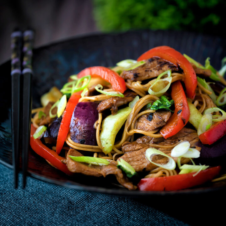 Hoisin pork stir fry with red peppers, onions and pak choi served in a dark bowl.