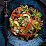 Overhead hoisin pork noodle stir fry with red peppers, onions and pak choi.