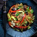 Overhead hoisin pork noodle stir fry with red peppers, onions and pak choi featuring a title overlay.