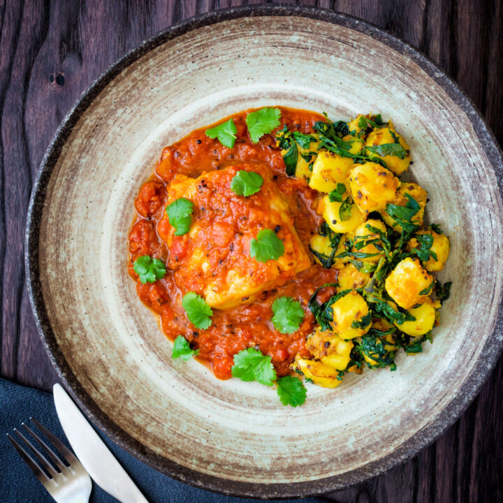 Macher jhol or Bengali fish curry served with aloo methi and fresh coriander.