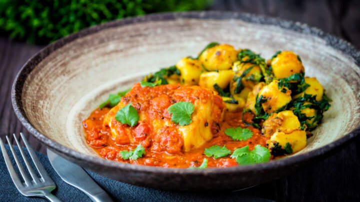 Macher jhol or Bengali fish curry served with aloo methi and fresh coriander.