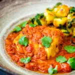 Close up macher jhol or Bengali fish curry served with aloo methi featuring a title overlay.