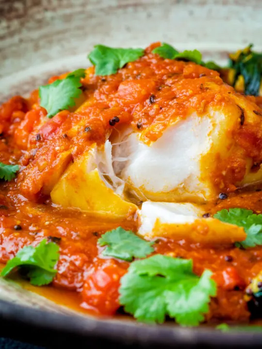 Macher jhol or Bengali fish curry with the fish cut open to show the white flesh flakes.