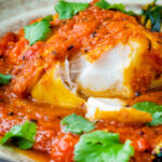 Macher jhol or Bengali fish curry with the fish cut open to show the white flesh flakes featuring a title overlay.