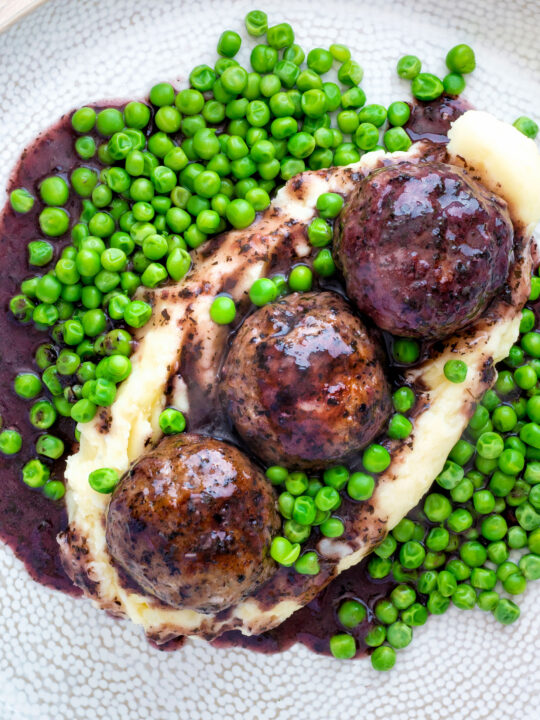 Overhead minted lamb meatballs with red wine gravy served with mashed potato and peas.