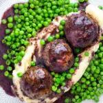 Overhead minted lamb meatballs with red wine gravy served with mashed potato and peas featuring a title overlay.