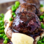 Close up minted lamb meatballs with red wine gravy served with mashed potato and peas.