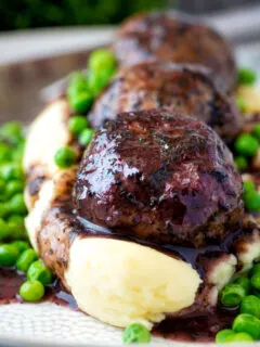 Close up minted lamb meatballs with red wine gravy served with mashed potato and peas.