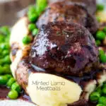 Close up minted lamb meatballs with red wine gravy served with mashed potato and peas featuring a title overlay.