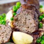 Cut open minted lamb meatball with red wine gravy served with mashed potato and peas.