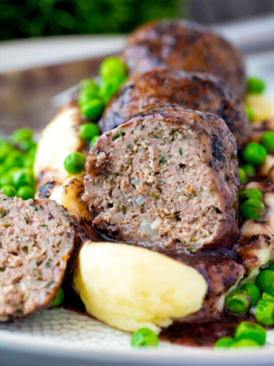 Cut open minted lamb meatball with red wine gravy served with mashed potato and peas.