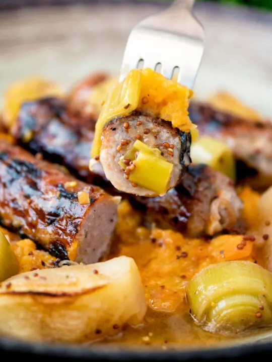 A piece of sausage from a sausage and apple casserole served with swede and carrot mash.