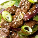 Close up black pepper beef stir fry with green pepper and red onion featuring a title overlay.