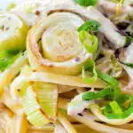 Close up chicken and leek pasta with linguini and shredded spring onions featuring a title overlay.
