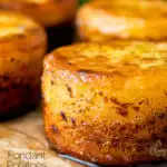 Close up fondant potatoes poached in butter and stock with a sprig of thyme featuring a title overlay.