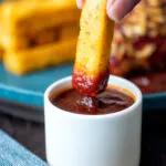 Crispy Fried polenta chip dipped in a pot of BBQ sauce.