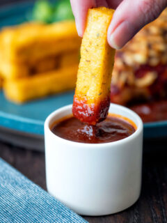 Crispy Fried polenta chip dipped in a pot of BBQ sauce.