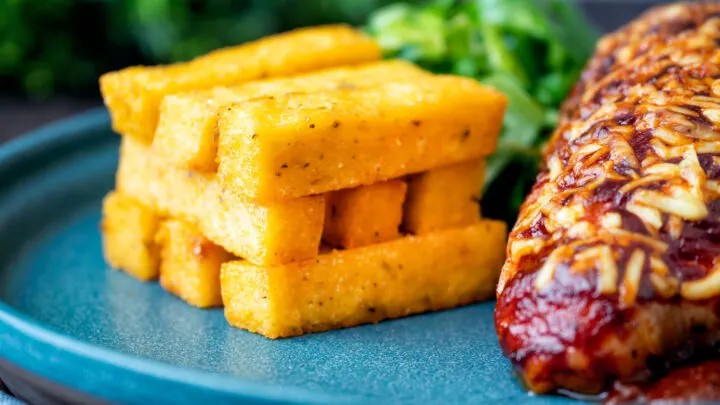 Stack of fried polenta chips with green salad and BBQ hunter chicken breast.