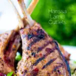 Close up harissa lamb chops served on a bed of herby buttered couscous featuring a title overlay.