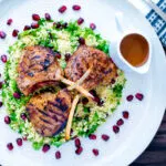 Overhead harissa lamb chops served on herby buttered couscous with a spicy sauce.