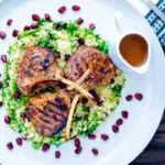 Overhead harissa lamb chops served on herby buttered couscous with a spicy sauce featuring a title overlay.