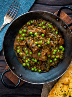Overhead methi gosht (beef and fenugreek) curry with peas served in an iron karai.
