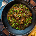 Overhead methi gosht (beef and fenugreek) curry with peas served in an iron karai featuring a title overlay.