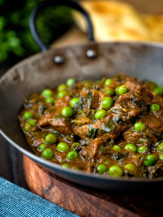 Close up methi gosht (beef and fenugreek) curry with peas served in an iron karahi.