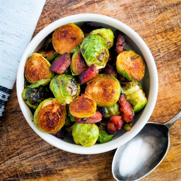 Roasted miso Brussel sprouts with bacon served in a white bowl.