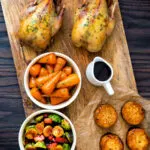 Overhead roast partridges served on a board with vegetables.
