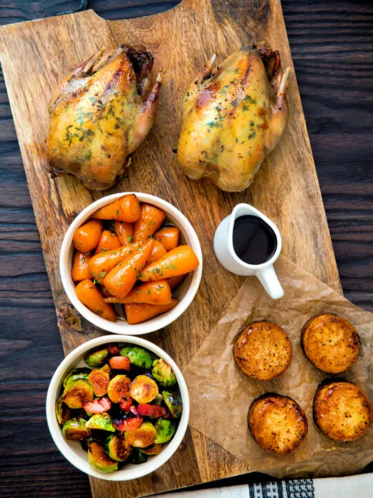 Overhead roast partridges served on a board with vegetables.