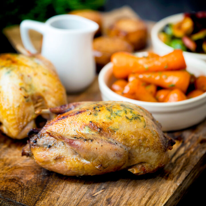Whole roast partridges served with vegetables on a board.