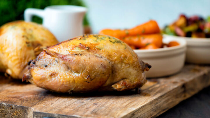 Whole roast partridges served with vegetables on a board.