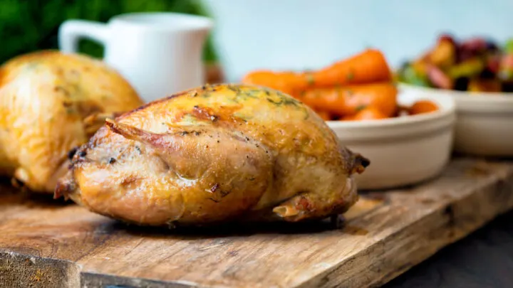 Whole roast partridges served with vegetables on a board.