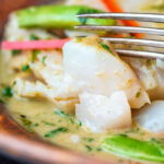 Close up Thai green fish curry showing big flakes of perfectly cooked cod.