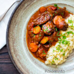 Overhead Moshari kokkinisto a Greek beef and tomato stew served with celeriac mash featuring a title overlay.