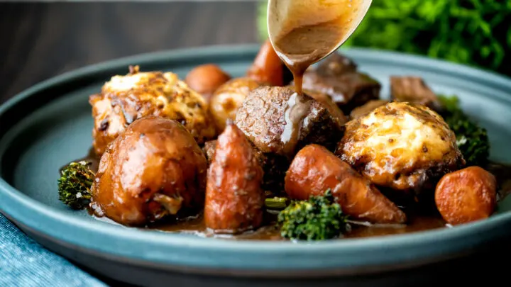 Gravy being poured over a British beef and ale stew with dumplings.