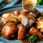 Gravy being poured over a British beef stew with dumplings.