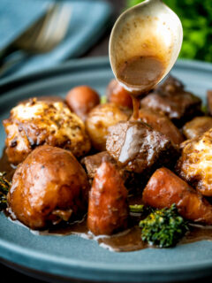 Gravy being poured over a British beef stew with dumplings.