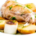 Close up braised rabbit legs served with leek rings and potatoes.