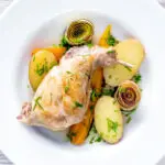 Overhead braised rabbit legs served with leek rings, carrots and potatoes.