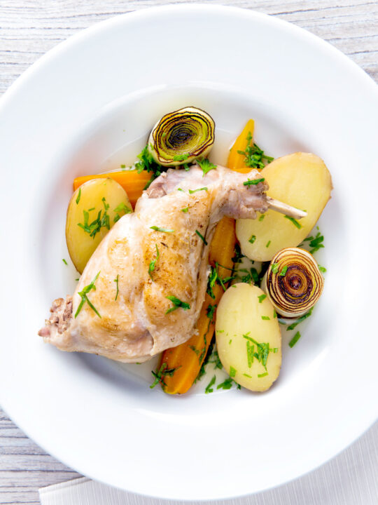 Overhead braised rabbit legs served with leek rings, carrots and potatoes.