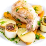 Braised rabbit legs served with leek rings, carrots and potatoes.