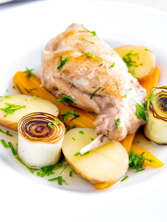 Braised rabbit legs served with leek rings, carrots and potatoes.