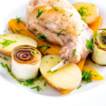 Braised rabbit legs served with leek rings, carrots and potatoes featuring a title overlay.