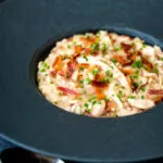 Creamy chicken and bacon risotto with snipped chives served in a black bowl.