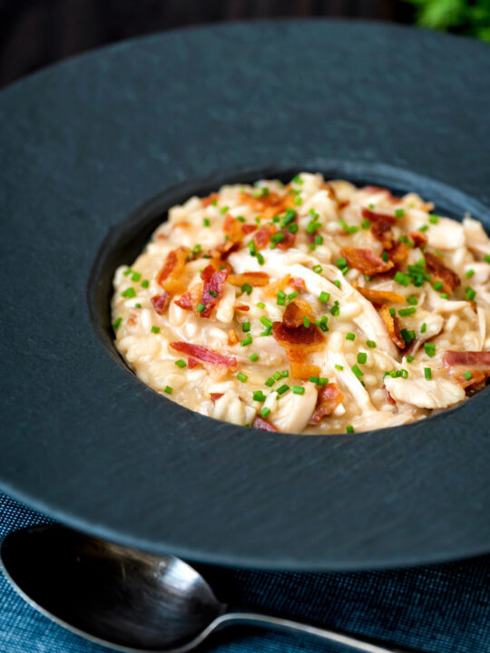 Creamy chicken and bacon risotto with snipped chives served in a black bowl.