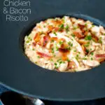 Creamy chicken and bacon risotto with snipped chives served in a black bowl featuring a title overlay.