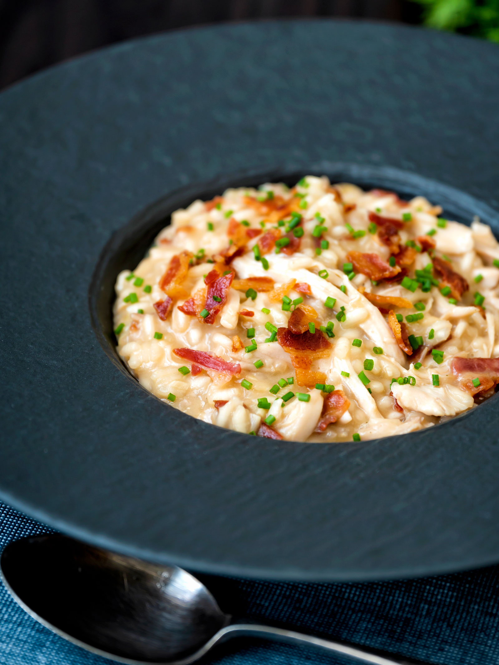 Creamy chicken and bacon risotto with snipped chives served in a black bowl.