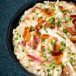 Close up creamy chicken and bacon risotto with snipped chives served in a black bowl.